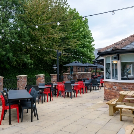 The exterior beer garden seating area at The Stanley Ferry, with wooden picnic tables, shade umbrellas, and string lights.