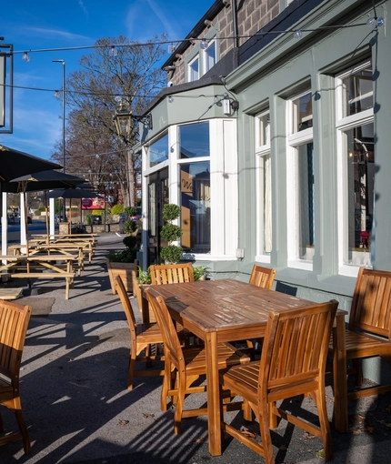 The exterior facade, signage, and seating area of The Horsforth, with wooden picnic tables, shade umbrellas, and string lights overhead.