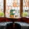 A close up view of a circular restaurant table with an upholstered U-shaped booth seat in a small leaded, bay window at The Talbot. Menus, salt and pepper mills, and a tealight stand on the table; and two potted plants sit on the windowsill.