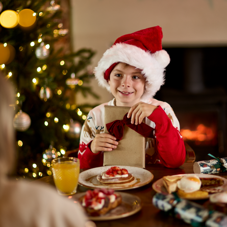 An image of an adult and child holding a gift while enjoying fruit juice and dishes from the Breakfast with Santa menu at Chef & Brewer venues.