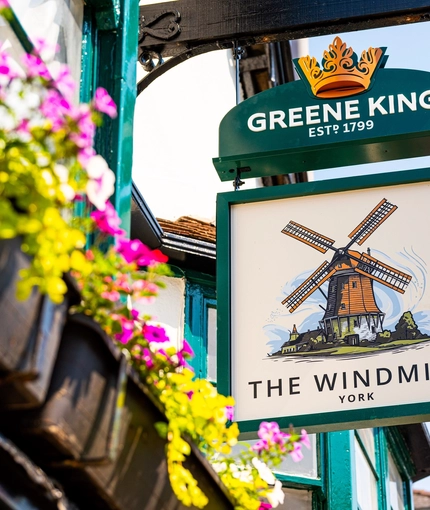 A close up view of the pub sign on the exterior wall of The Windmill Inn. The sign features an illustration of a windmill above the words "The Windmill, York", on a white background.