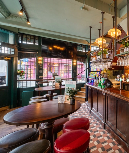 The bar and interior restaurant seating area at The Golden Lion in Soho, with a TV on the wall, a gaming machine, and glasses hanging in racks above the counter.