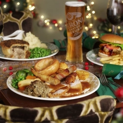 An advertising image of 3 plated Xmas Day Main dishes with a selection of drinks sat on a table within the interior restaurant seating available at Proper Locals venues.