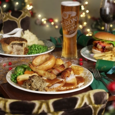 An advertising image of 3 plated Xmas Day Main dishes with a selection of drinks sat on a table within the interior restaurant seating available at Proper Locals venues.