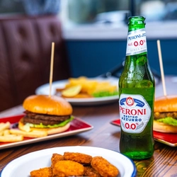 A bowl of chicken nuggets and dipping sauce sitting on a table next to other plates of food and a bottle of Peroni low alcohol beer.