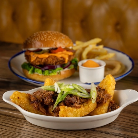 A roasting dish containing Loaded BBQ Hot Honey Hash Browns on an indoor wooden table.