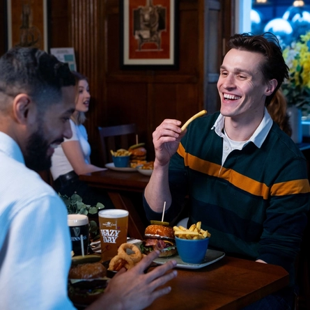 Two people sat in the interior restaurant and seating area in a Urban Social venue, enjoying burger main meals and drinks.