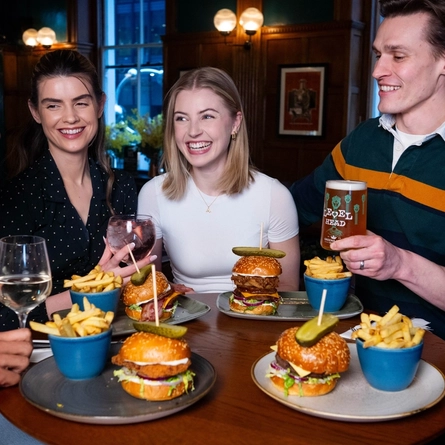 A group of friends sat in the interior restaurant and seating area in a Urban Social venue, enjoying burger main meals and drinks.