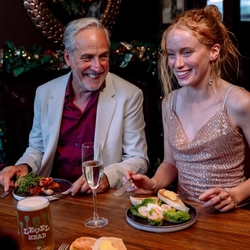 An image showing 2 people sat at a table with other enjoying New Years Eve food and drinks within the interior restaurant seating area at a Community Social venue.