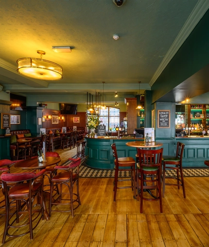 The bar and interior restaurant seating area at The Globe; with checkerboard tiles in front of the counter, wood panelled walls, bar stool seating, and TVs on the walls.