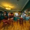 The bar and interior restaurant seating area at The Globe; with checkerboard tiles in front of the counter, wood panelled walls, bar stool seating, and TVs on the walls.