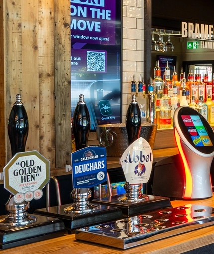 A close up view of the bar inside The Bramford Arms in Woodsetton, with a TV on the wall above the counter.
