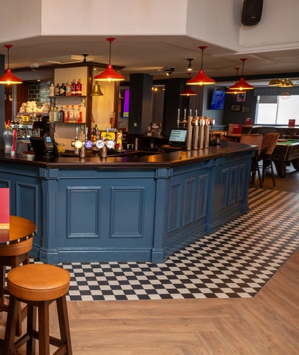 The bar and interior restaurant seating area at the Devonshire Arms, with checkerboard patterned floor, and bar stool seating.