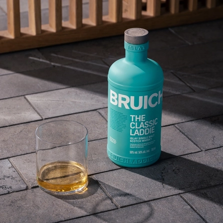 A bottle and a glass of Bruichladdich The Classic Laddie whisky, standing on a paved stone floor.