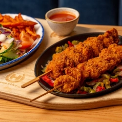 A  kebab skewer on a skillet, on an indoor table.