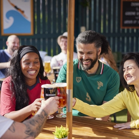 A mixed group of people seated at an outdoor table holding drinks.