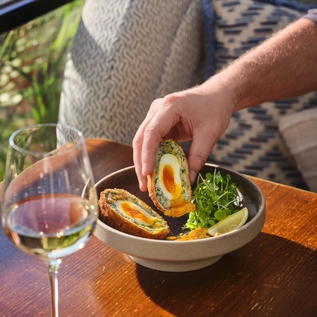 An exterior lifestyle image showing a customer sat at a table with a bowled Scotch Egg dish and a glass of white wine at The White Horses.