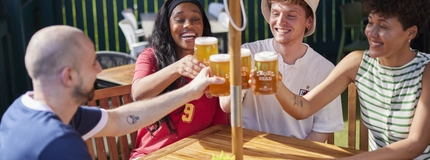 A mixed group of people seated at an outdoor table holding drinks.