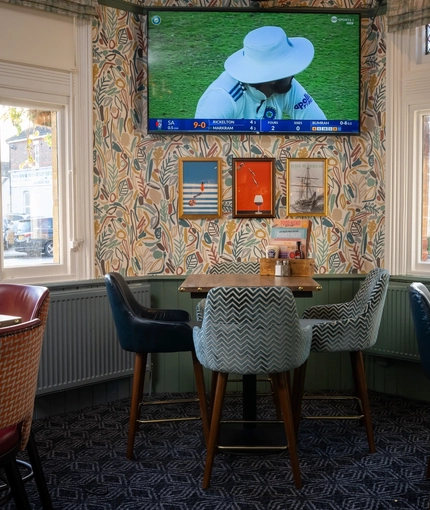 An interior restaurant seating area at the Green Posts, with a TV on the wall, and upholstered seats.