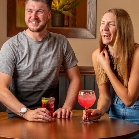 A man and a woman seated at an indoor table enjoying cocktails.