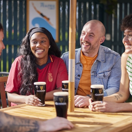 A mixed group of people seated at an outdoor table holding drinks.
