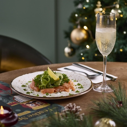 An advertising image showing a plate dish and a glass of sparkling white wine from the Festive Spread menu sat on a table within the interior restaurant seating area at a Chef & Brewer venue.