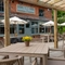 The paved exterior beer garden seating area at the Ye Olde Leathern Bottel in Barkham, with an under cover section, shade umbrellas, potted plants on each table, and string lights overhead.