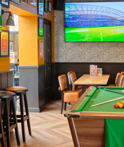 The interior pub gaming area at The Carousel, with a pool table, dartboard, TVs on the walls, stool seating and a restaurant table.
