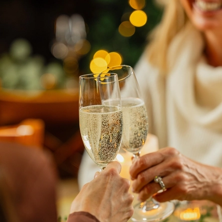 An image of 2 customers holding 2 glasses of sparkling white wine celebrating with a festive cheers over Christmas at Venture Hotels.