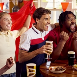A group of friends sat round a table with drinks and small plates of food enjoying watching a sports event at a Flaming Grill venue.