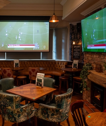 The interior restaurant seating area with tables, chairs, multiple TV screens and brick log burner fireplace at The Church View Inn.