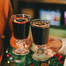 Two people in a pub bar area, holding glasses of mulled wine garnished with orange slices.