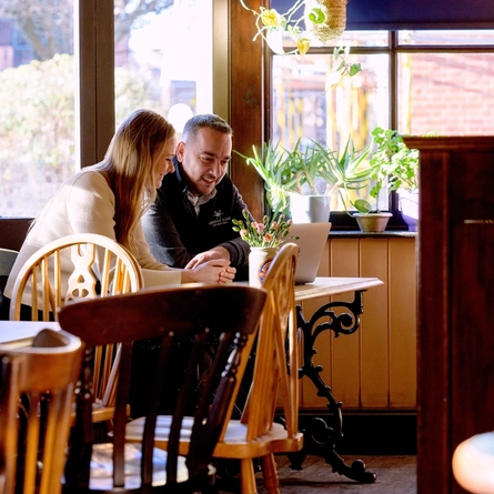 A Woman and a Man are sat on a table looking at a laptop