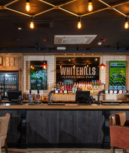The bar and interior restaurant seating area at Whitehills in Northampton, with TVs on the walls, and upholstered seats.