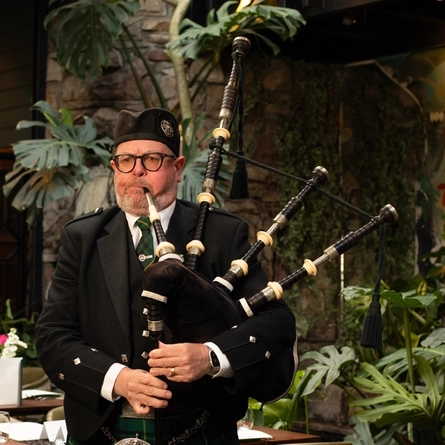 A Bagpipe Player stood within the interior restaurant seating area at The Ubiquitous Chip.