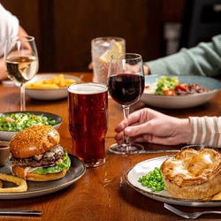 A hand holding a glass of wine on a table with two plates of food in front of it.