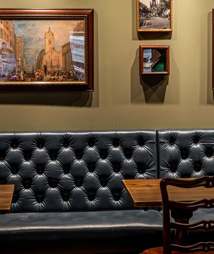 An interior restaurant seating area at The Beehive Inn, with a long, upholstered booth seat, wooden tables, and framed artwork on the walls.