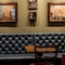 An interior restaurant seating area at The Beehive Inn, with a long, upholstered booth seat, wooden tables, and framed artwork on the walls.