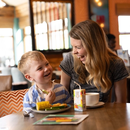 An image showing a parent enjoying a hot drink sat at a table with a child enjoying a child's meal and carton of juice within the interior restaurant seating area at a Flaming Grill venue.