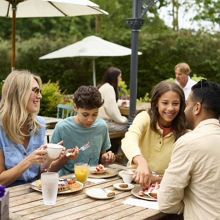 An image of a family enjoying various dishes and drinks within the exterior beer garden seating area at a Chef & Brewer venue.
