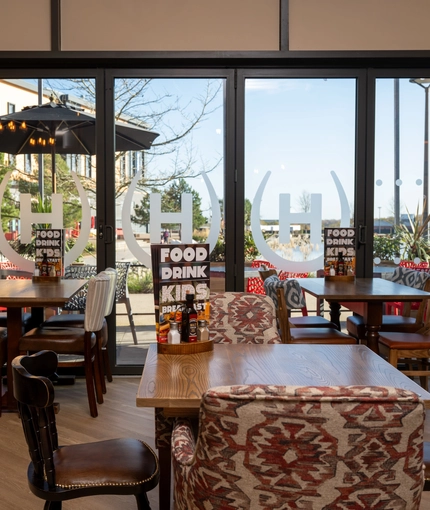 An interior restaurant seating area at The Wrekin Giant, with floor-length windows looking onto the exterior beer garden seating area and the surrounding buildings.