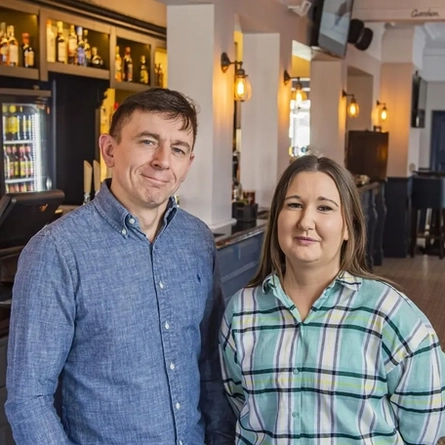 Two people standing in the restaurant of a pub.