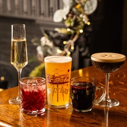 A glass of sparkling wine, a cocktail served in a whiskey glass, a pint of Hazy Day served in a branded pint glass, a glass mug of mulled wine, and an Espresso Martini; standing on the bar inside a pub.