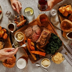 An image of a people enjoying a Sunday Roast sharing platter dish with sides and a selection of drinks within the interior restaurant seating area at The Foundry Bell.