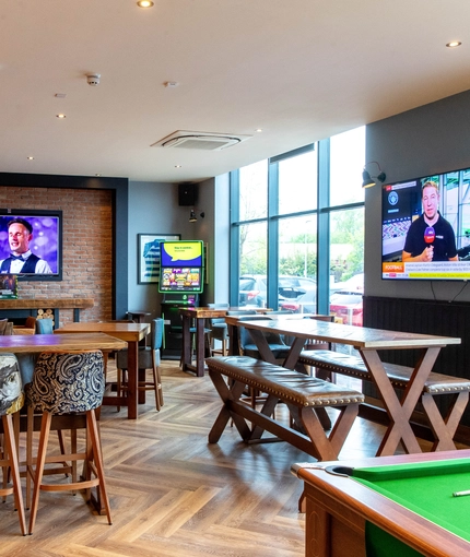 Interior dining area of a pub with a fireplace, a pool table, a gambling machine and a few TVs.