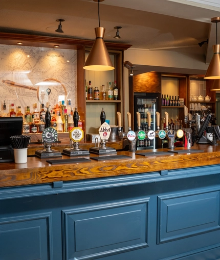 The bar inside The Horsforth, with a checkerboard floor, and bottles of alcohol on wooden shelves behind the counter.