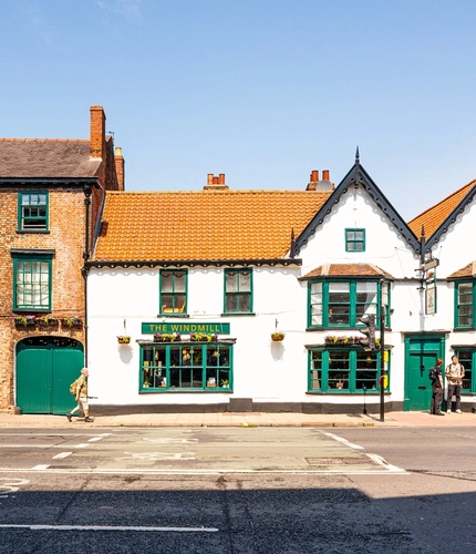 A view from across the road of the exterior facade and signage of The Windmill Inn in York, with flower baskets hanging on the wall.