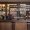 A close up view of the bar at The Man On The Moon, showing the beer taps, bottles of various spirits and wines on shelves, and glasses hanging in racks above the bar.