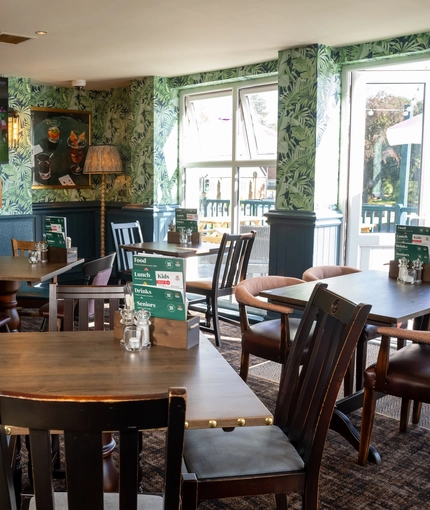 An interior restaurant seating area at the Rudds Arms; with a TV on the wall, and doors leading to the exterior seating area on the deck.