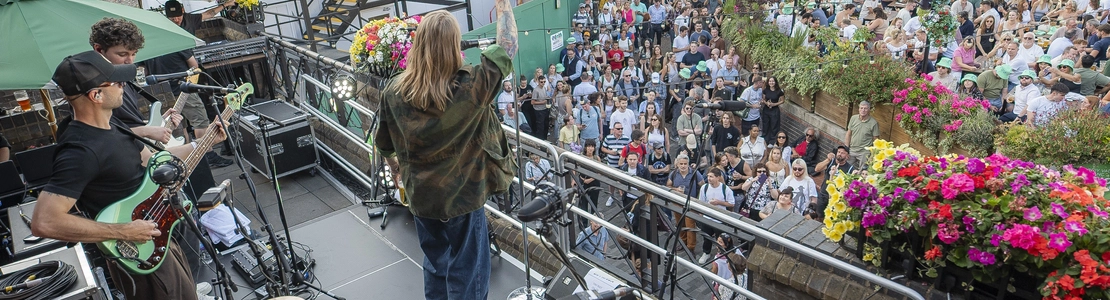 An image of Sam Ryder and his band performing a surprise gig on an exterior Live Event Stage with an audience to promote the Live At Your Local competition at The Anchor Bankside.